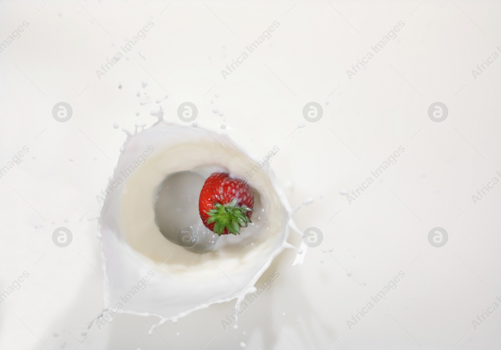 Photo of Strawberry falling in milk with splash, top view