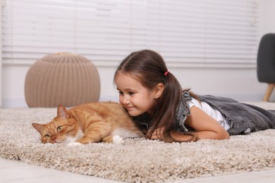 Smiling little girl and cute ginger cat on carpet at home