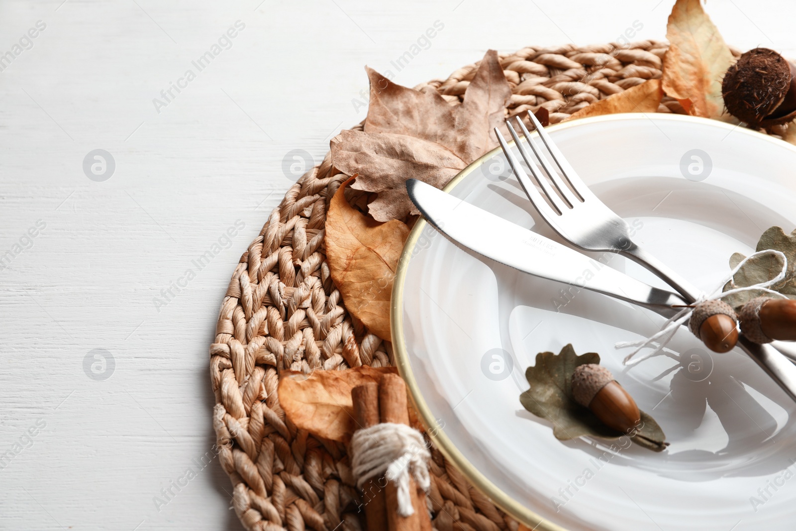 Photo of Autumn table setting with dry leaves on wicker mat, closeup