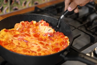 Photo of Man cooking tasty fried eggs with tomatoes on stove, closeup