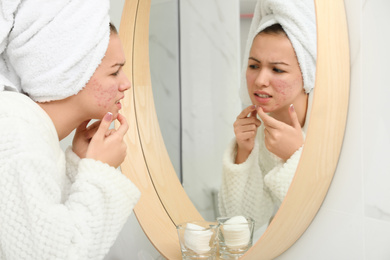 Photo of Teen girl with acne problem squeezing pimple near mirror in bathroom