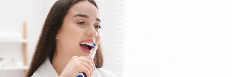 Happy woman using electric toothbrush in bathroom. Banner design with space for text