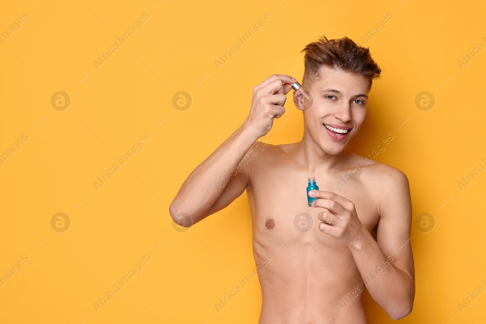 Photo of Handsome man applying serum onto his face on orange background. Space for text