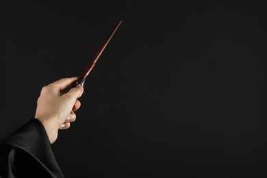 Photo of Wizard holding magic wand on black background, closeup. Space for text