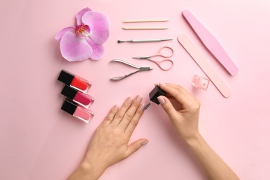 Woman applying nail polish on color background, top view