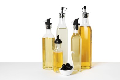 Photo of Bottles of different cooking oils and olives on white background