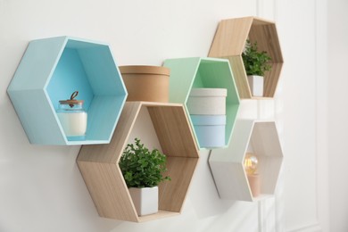 Photo of Honeycomb shaped shelves with decorative elements and houseplants on white wall