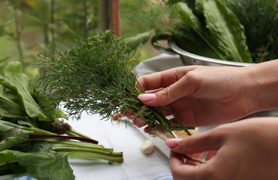 Photo of Woman with fresh green herbs and twine indoors, closeup