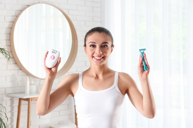 Photo of Beautiful young woman with epilator and razor indoors