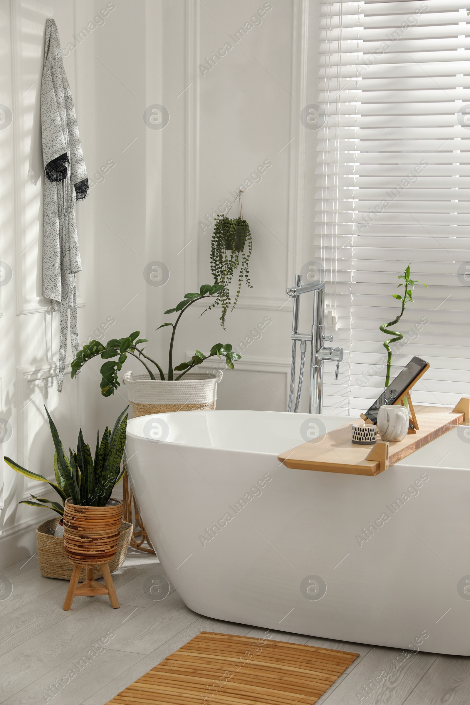 Photo of Stylish white tub and green houseplants in bathroom. Interior design