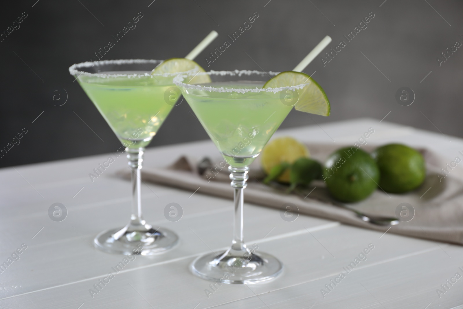 Photo of Delicious Margarita cocktail in glasses, lime and bar spoon on white wooden table