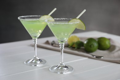 Delicious Margarita cocktail in glasses, lime and bar spoon on white wooden table