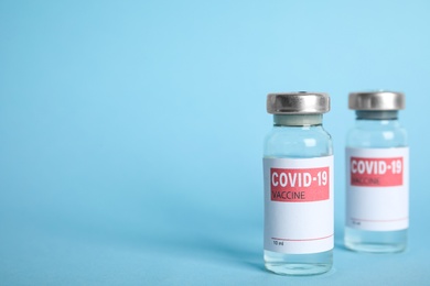 Photo of Vials with coronavirus vaccine on light blue background, space for text