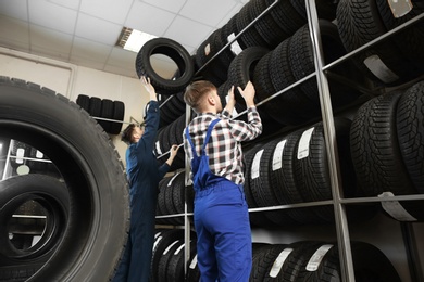Young male mechanics with car tires in automobile service center