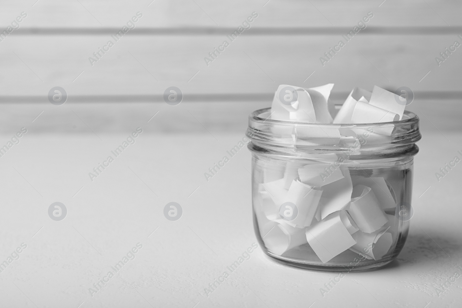 Photo of Glass jar with paper pieces on white table, space for text