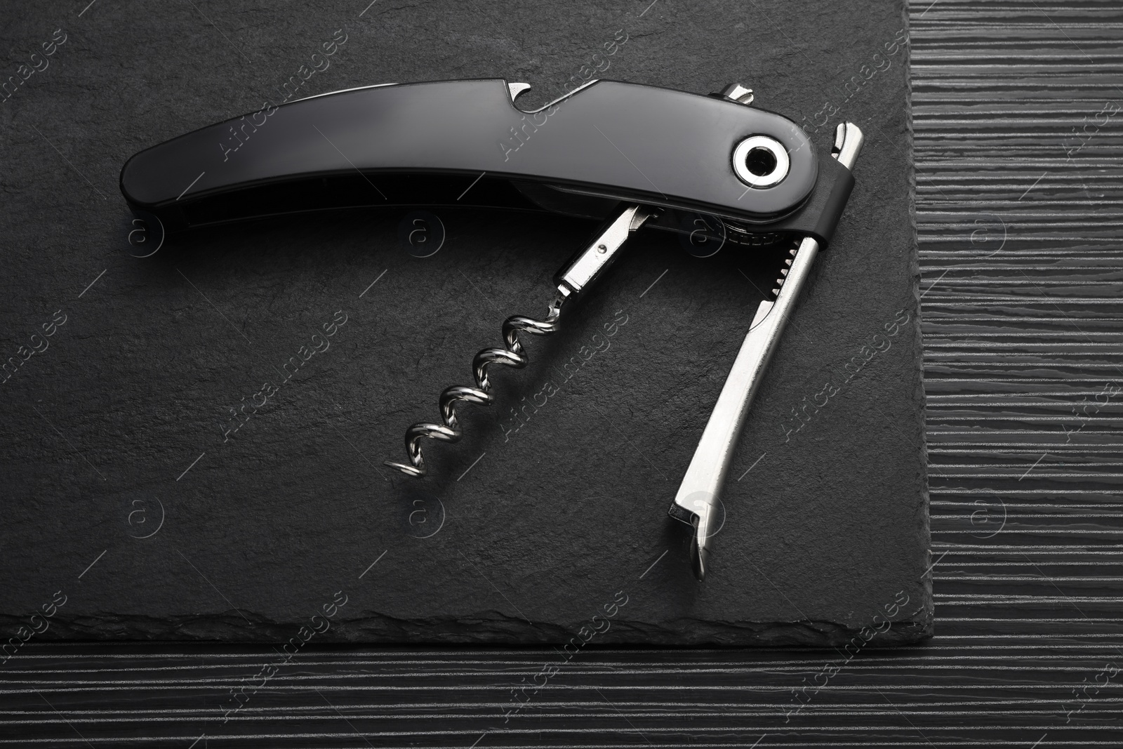 Photo of One corkscrew (sommelier knife) on black wooden table, top view