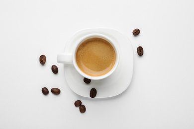 Scattered coffee beans and cup of hot espresso isolated on white, top view