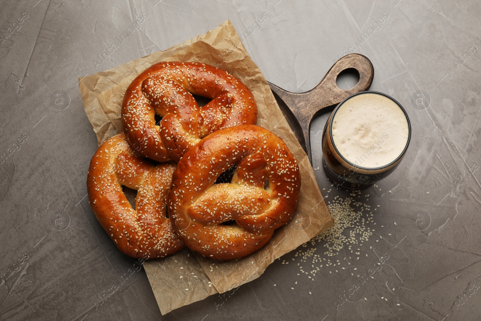 Photo of Tasty pretzels and glass of beer on grey table, flat lay