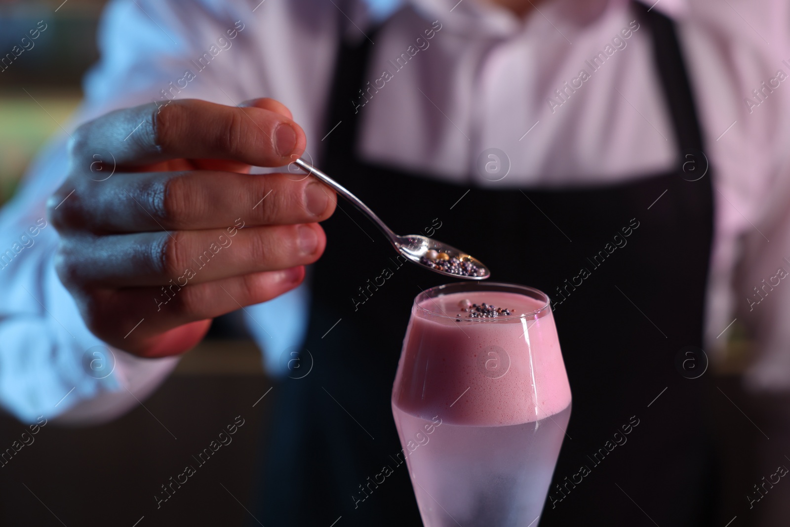 Photo of Bartender decorating fresh alcoholic cocktail with sprinkles on blurred background, closeup