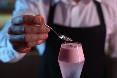 Photo of Bartender decorating fresh alcoholic cocktail with sprinkles on blurred background, closeup
