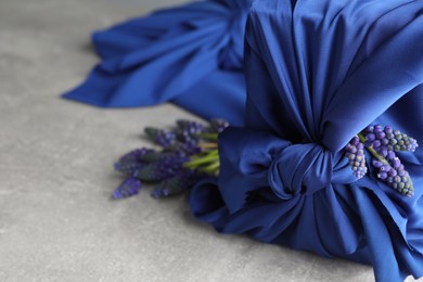 Photo of Furoshiki technique. Gift packed in blue silk fabric and muscari flowers on light grey table, closeup. Space for text