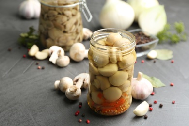 Photo of Glass jar of pickled mushrooms and ingredients on grey table. Space for text