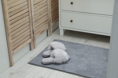 Photo of Grey mat with slippers near chest of drawers indoors