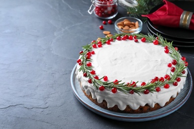 Traditional Christmas cake decorated with rosemary and cranberries on dark grey table, space for text