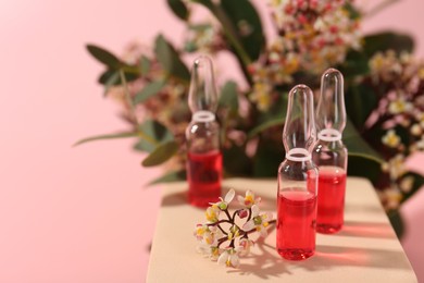 Stylish presentation of skincare ampoules and flowers on pink background, closeup. Space for text