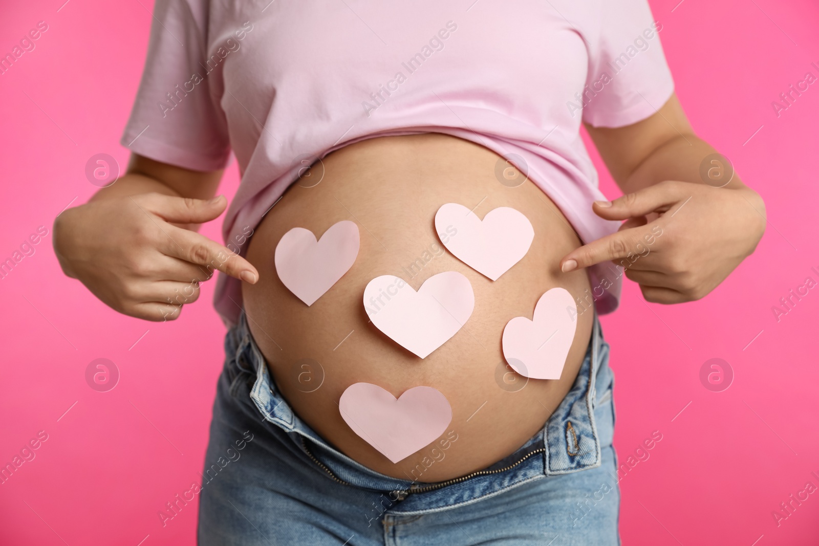 Photo of Pregnant woman with heart shaped sticky notes on belly against pink background, closeup. Choosing baby name