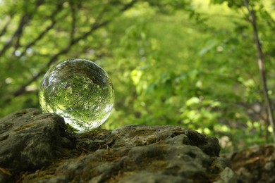 Beautiful green trees outdoors, overturned reflection. Crystal ball on stone in forest. Space for text