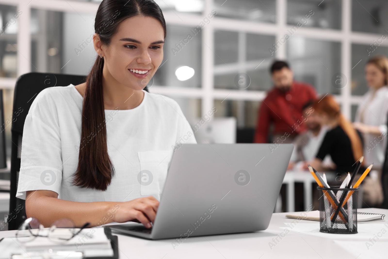 Photo of Team of employees working together in office. Happy woman with laptop at table indoors