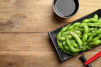 Photo of Green edamame beans in pods served with soy sauce on wooden table, flat lay. Space for text