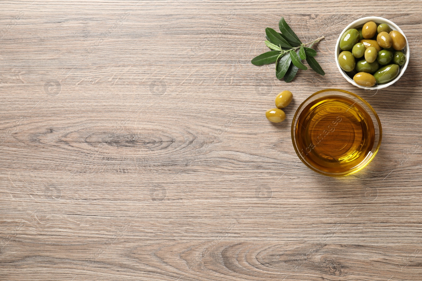 Photo of Glass bowl of oil, ripe olives and green leaves on wooden table, flat lay. Space for text