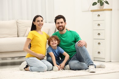 Family portrait of pregnant mother, father and son sitting on floor in house