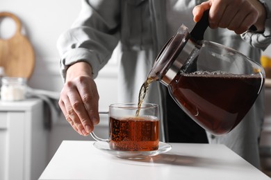 Photo of Woman pouring hot tea into cup at white table, closeup