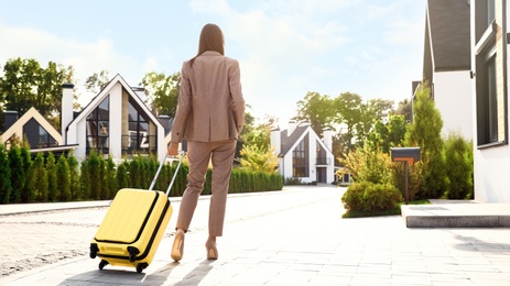 Photo of Young businesswoman with suitcase outdoors, back view. Moving day