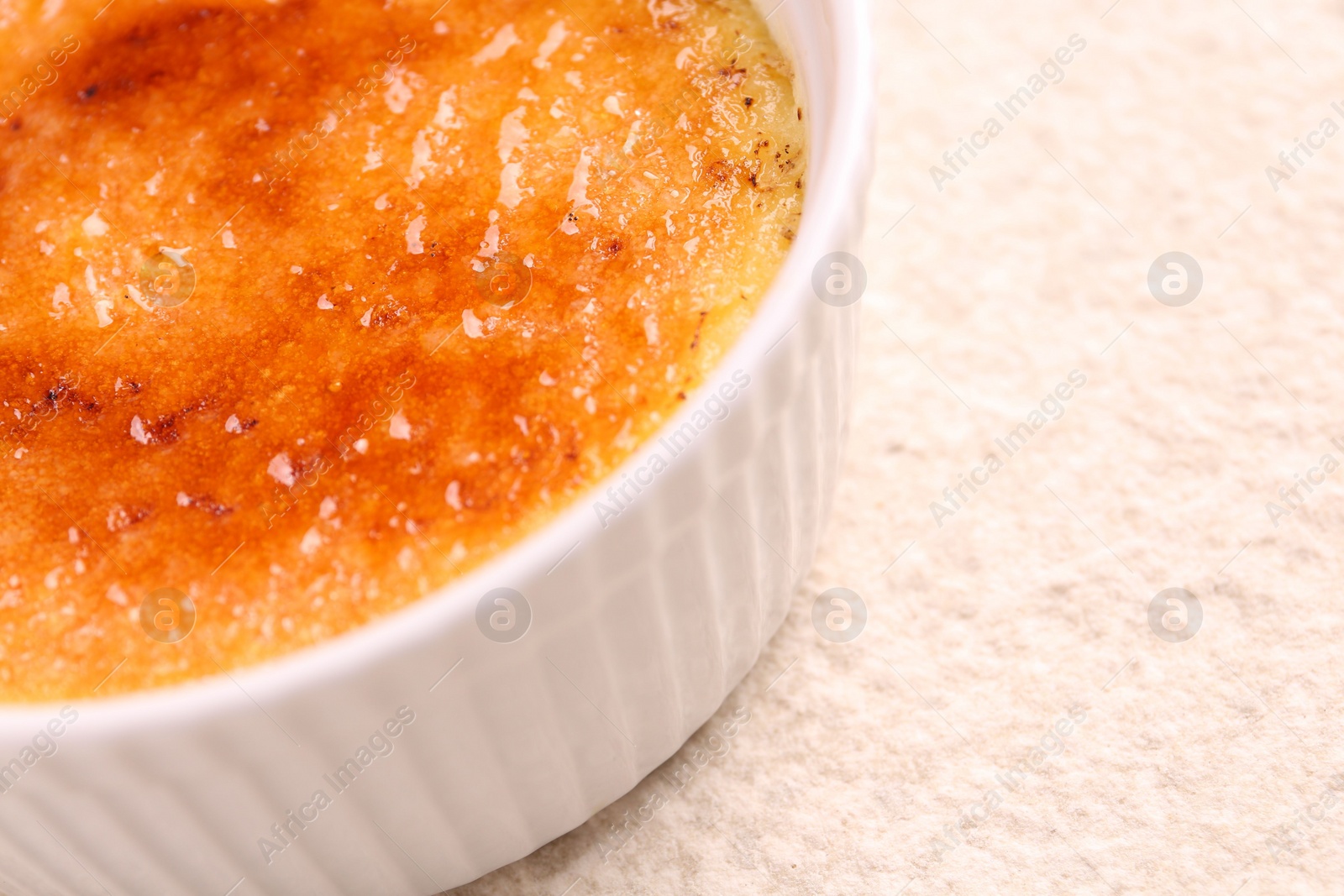 Photo of Delicious creme brulee in bowl on light textured table, closeup. Space for text