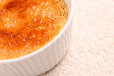 Delicious creme brulee in bowl on light textured table, closeup. Space for text