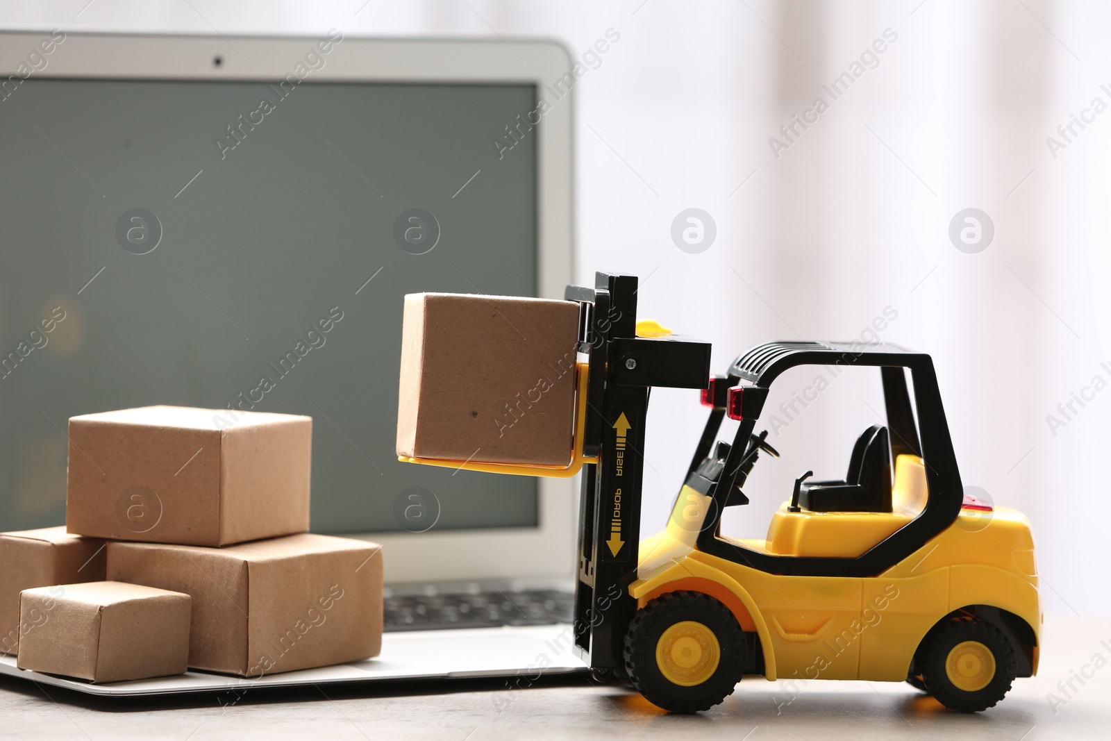 Photo of Toy forklift with box near laptop on table. Logistics and wholesale concept