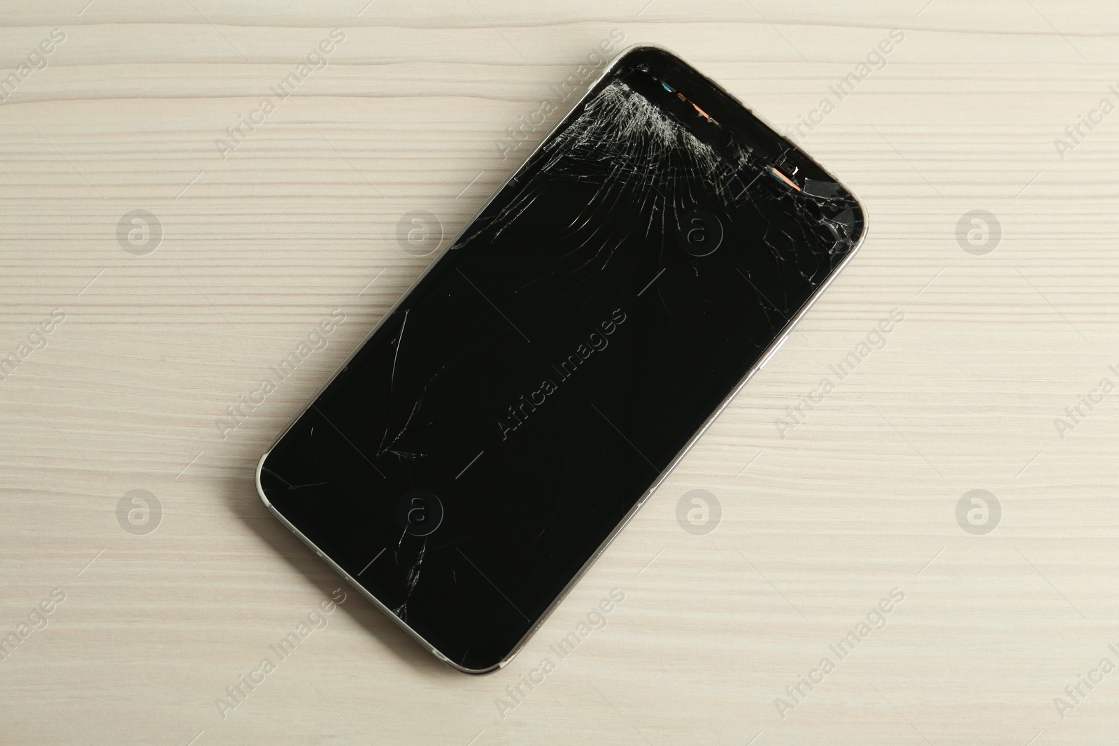 Photo of Smartphone with cracked screen on white wooden table, top view. Device repair