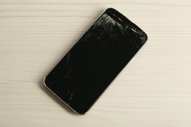 Smartphone with cracked screen on white wooden table, top view. Device repair