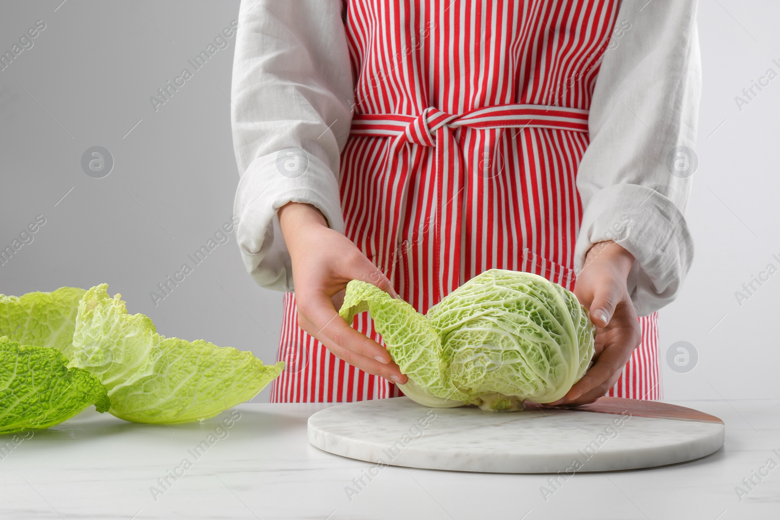 Photo of Woman separating leaf from fresh savoy cabbage at white marble table, closeup