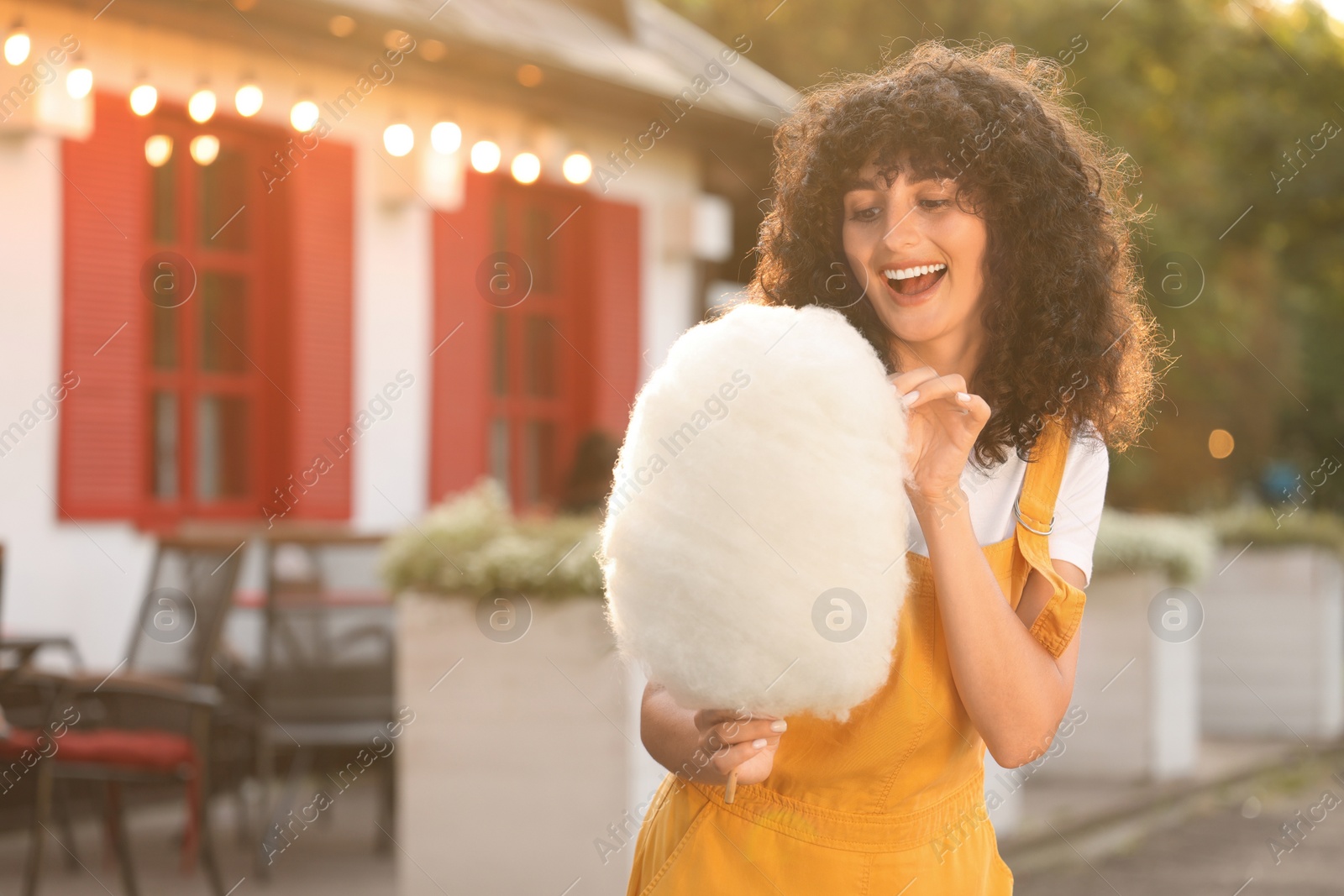 Photo of Happy woman with cotton candy outdoors on sunny day. Space for text