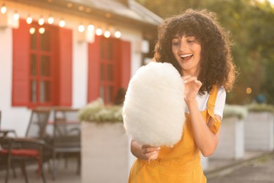 Happy woman with cotton candy outdoors on sunny day. Space for text