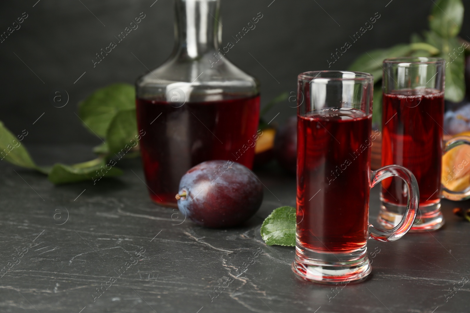 Photo of Delicious plum liquor and ripe fruits on black table. Homemade strong alcoholic beverage