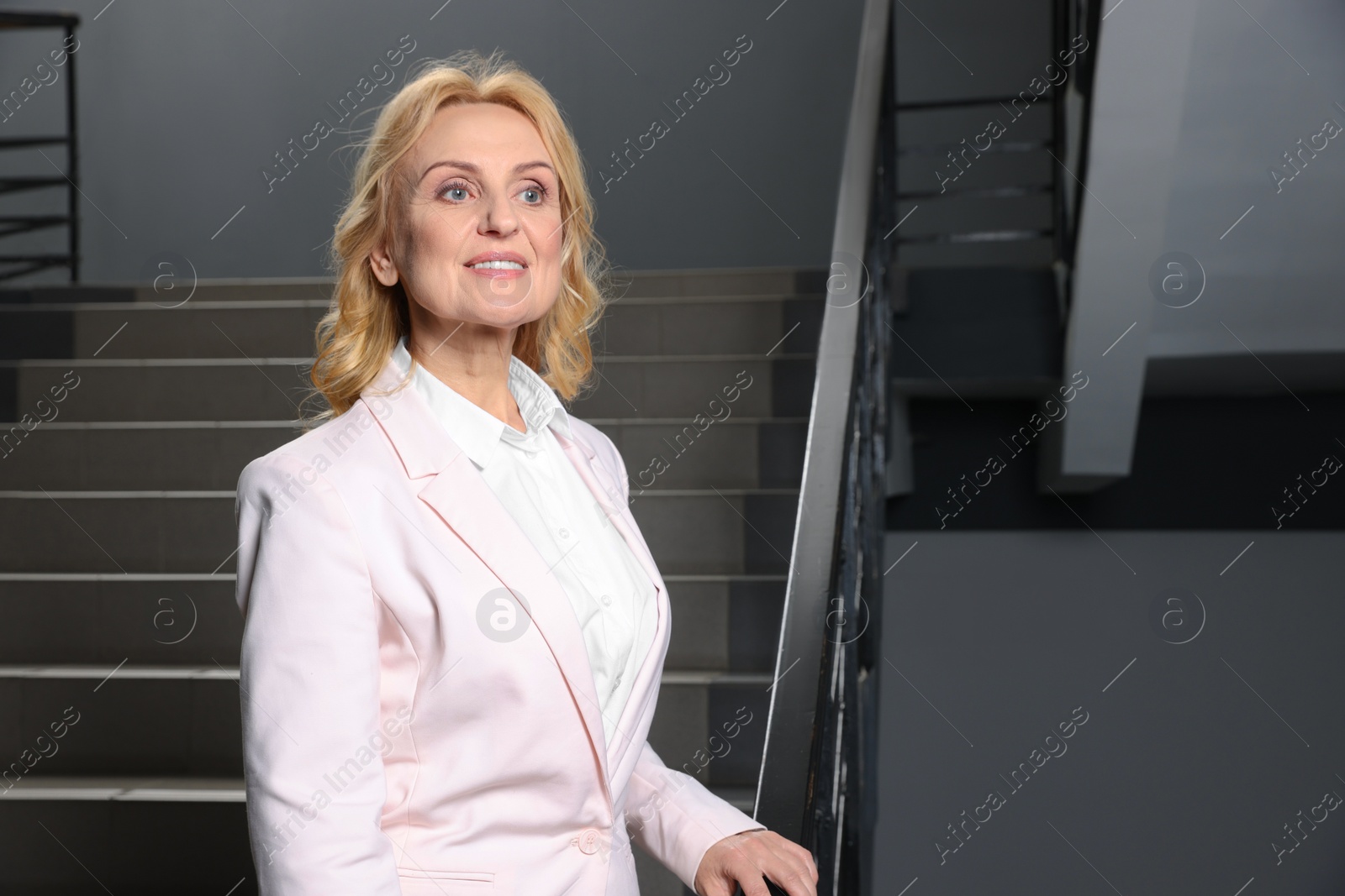 Photo of Happy lady boss near staircase indoors, space for text. Successful businesswoman