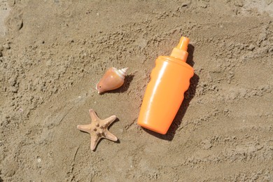 Blank bottle of sunscreen, starfish and seashell on sand, flat lay