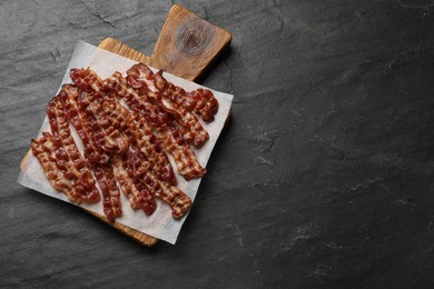 Photo of Slices of tasty fried bacon on black table, top view. Space for text