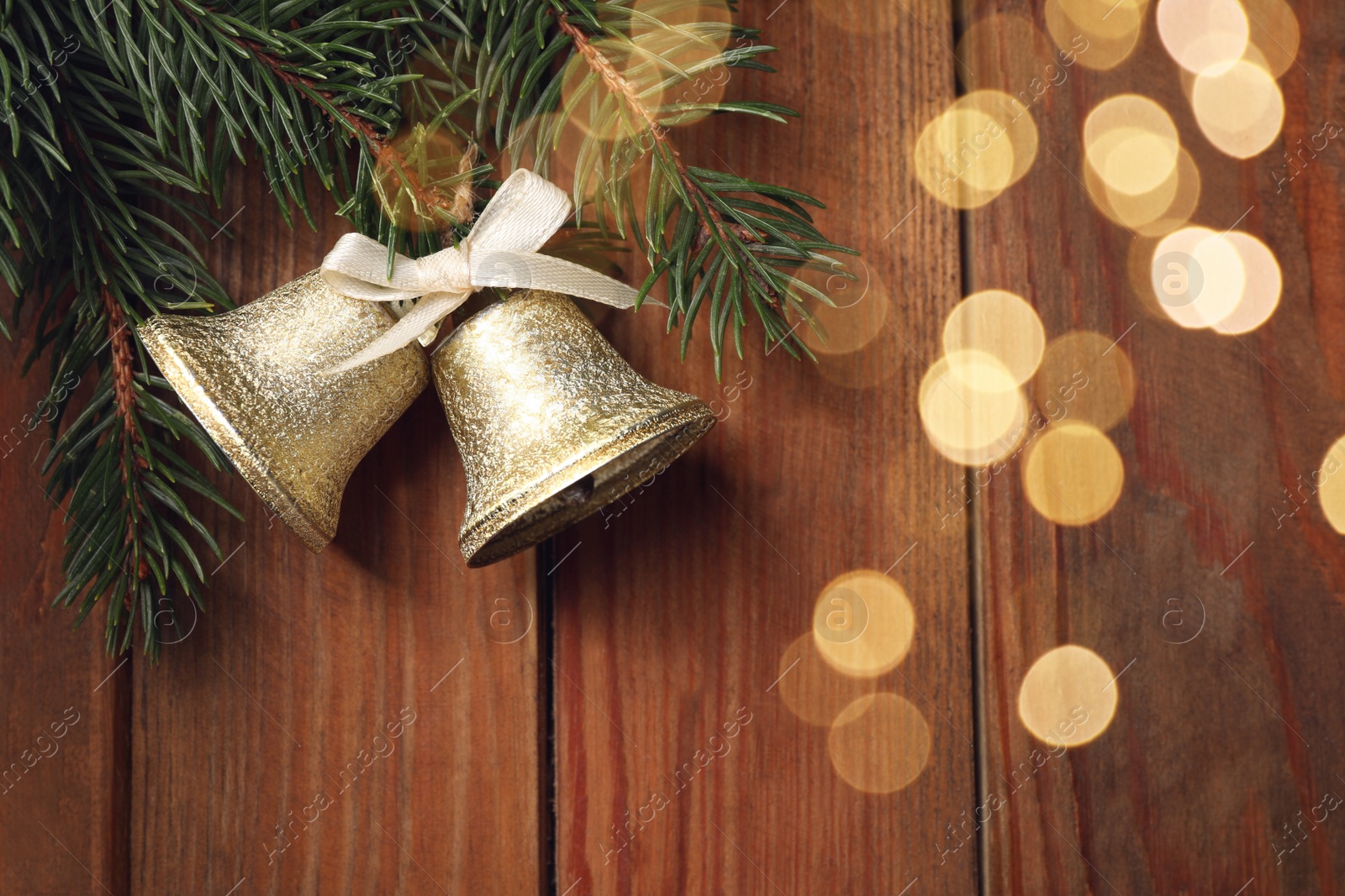 Photo of Christmas bells and fir tree branches on wooden table, flat lay. Space for text